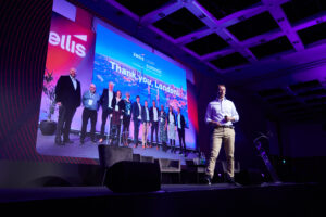 Zellis Chief Product Officer, George Dunnett, speaks on stage in front of an image of colleagues taken at the 2023 User Summit.